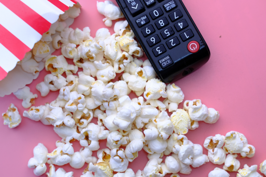 Popcorn in rot-weiß gestreifter Tüte auf rosa Untergrund, daneben schwarze Fernbedienung